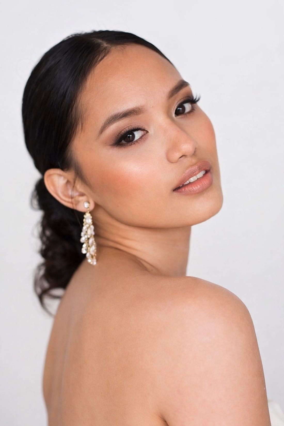 Mariée au chignon bas et boucles d'oreilles perlées, maquillage Studio Ayra